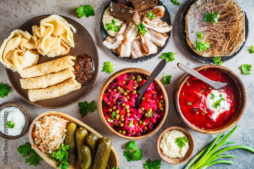 Traditional Russian cuisine concept. Borsch, jellied meat, lard, crepes, salad vinaigrette and sauerkraut, top view, gray background.