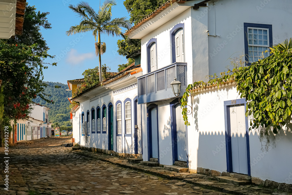 Obraz premium Historic colonial estate in white and blue with plants and palm tree in late afternoon sun in historic town Paraty, Brazil