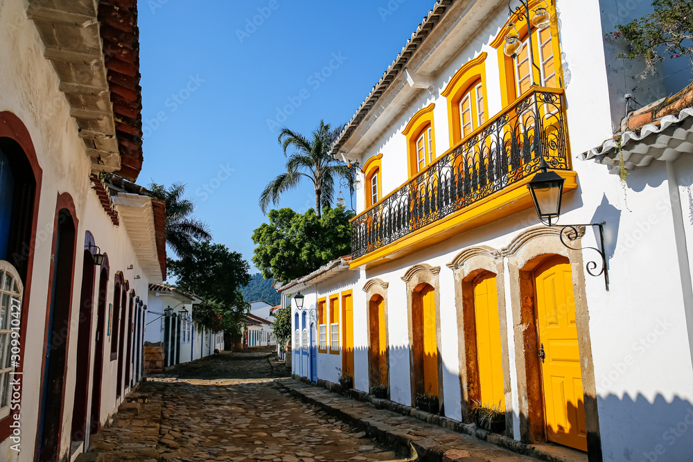 Narrow street with a wonderful colonial building with yellow wooden doors, windows and balustrade in late afternoon sun, historic town Paraty, Brazil