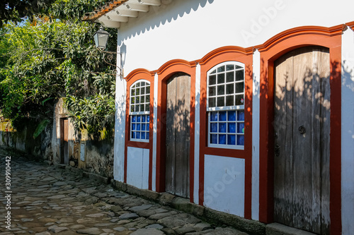 Artful white house facade with red framed windows and doors in late afternoon sun and shadows, historic town Paraty, Brazil