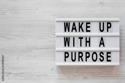 'Wake up with a purpose' words on a lightbox on a white wooden background, top view. Overhead, from above, flat lay. Copy space.