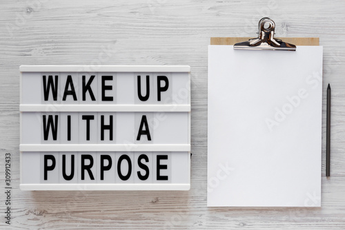 Fototapeta Naklejka Na Ścianę i Meble -  'Wake up with a purpose' words on a lightbox, clipboard with blank sheet of paper on a white wooden surface, top view. Overhead, from above, flat lay. Copy space.