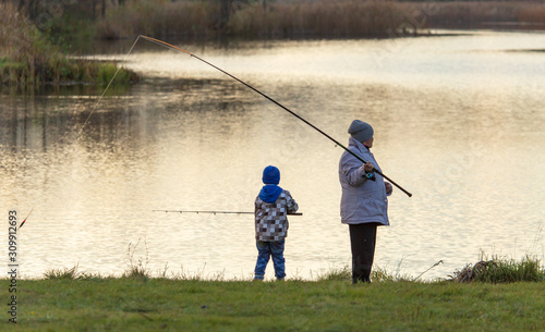 The boy with the grandmother catches fish in the pond at sunset
