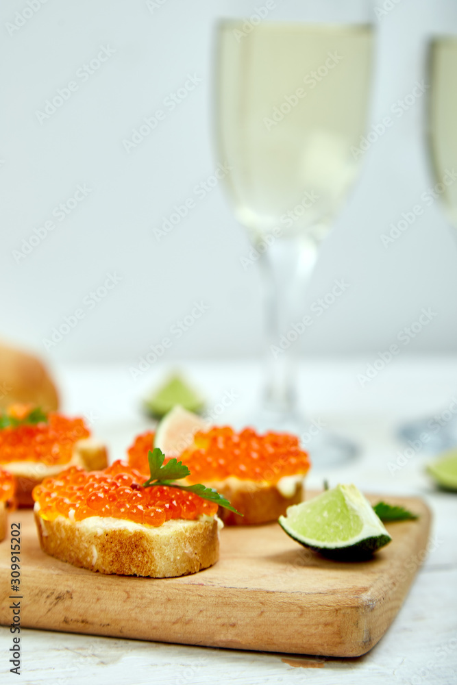 Salmon red caviar in bowl and Sandwiches with on wooden cutting board, glass with champagne on white background copy space. Salmon red caviar in bowl and Sandwiches with on wooden cutting board, glass with champagne on white background copy space.