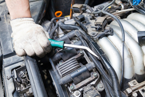 A car repairman unscrews parts with a wrench with a green handle in the engine compartment suh as spark plugs and ignition coils in a vehicle repair workshop. Auto service industry.