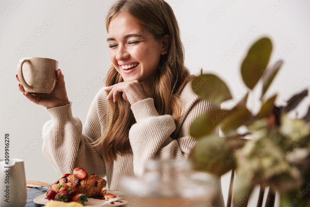 Image of laughing caucasian woman drinking tea while having breakfast - obrazy, fototapety, plakaty 