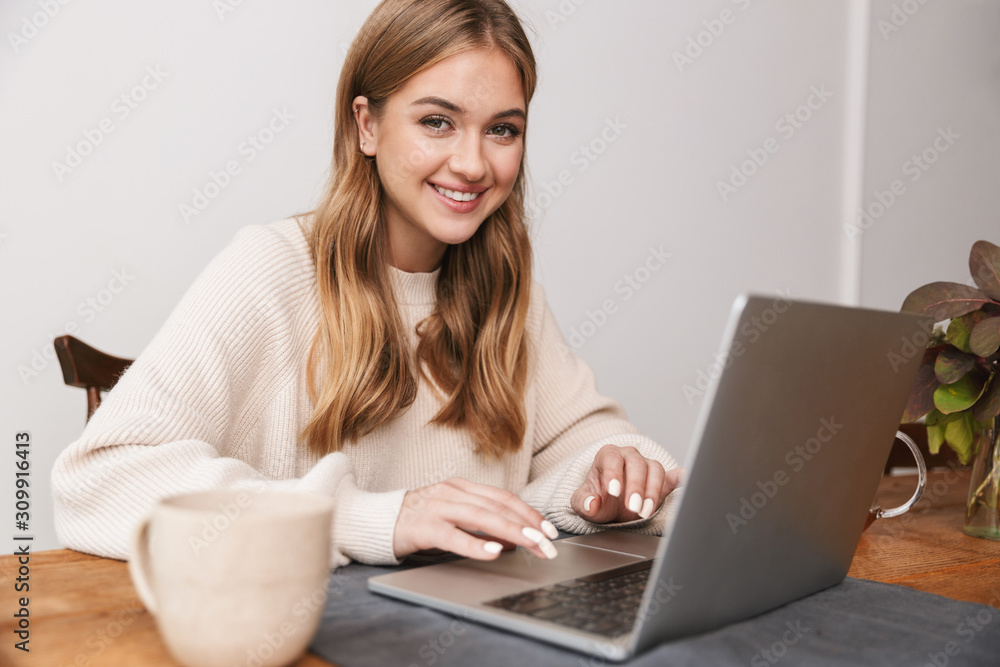 Image of smiling caucasian woman using laptop and drinking tea Image of smiling caucasian woman using laptop and drinking tea