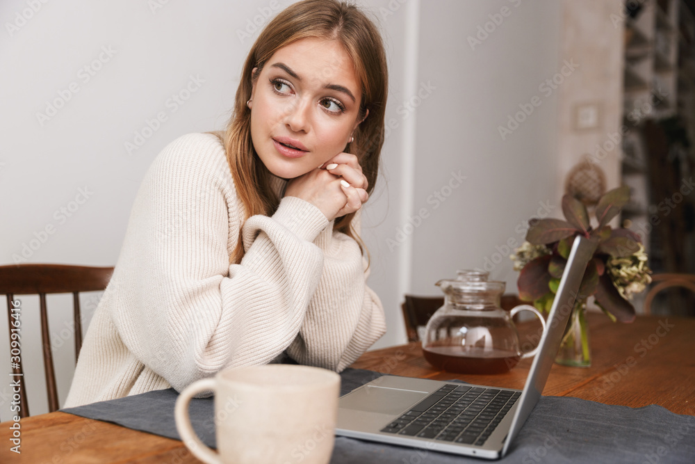Image of young caucasian woman using laptop and drinking tea Image of young caucasian woman using laptop and drinking tea