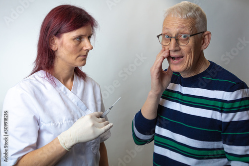 Close up of nurse and elderly man  patient. A nurse holds a syringe  a man is afraid
