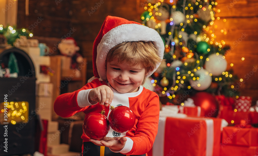 Happy child is wearing Santa clothes, decorating the Christmas tree hold bauble. Christmas concept. Santa helper kids. Happy child is wearing Santa clothes, decorating the Christmas tree hold bauble. Christmas concept. Santa helper kids.