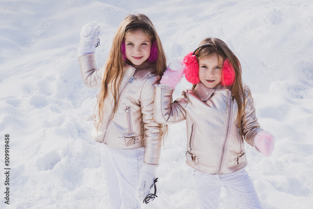 Children in Winter Park playing snowballs. Cute sisters playing in a snow. Winter clothing for baby and toddler. Little girls throw snowball in park.