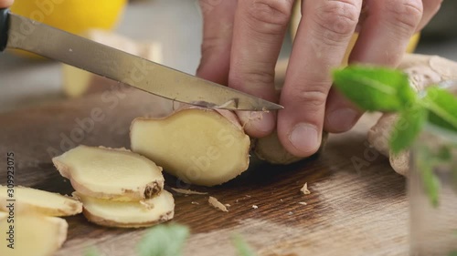 Male hand cuts ginger with a knife on a board for making lemonade. Tea or cocktail ingredients. Ginger root