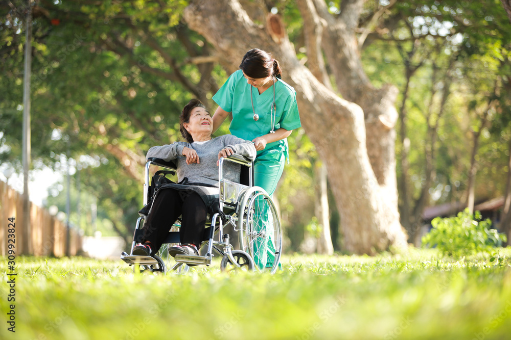 Asian senior woman sitting on the wheelchair with woman in doctor uniform in the park hospital Asian senior woman sitting on the wheelchair with woman in doctor uniform in the park hospital