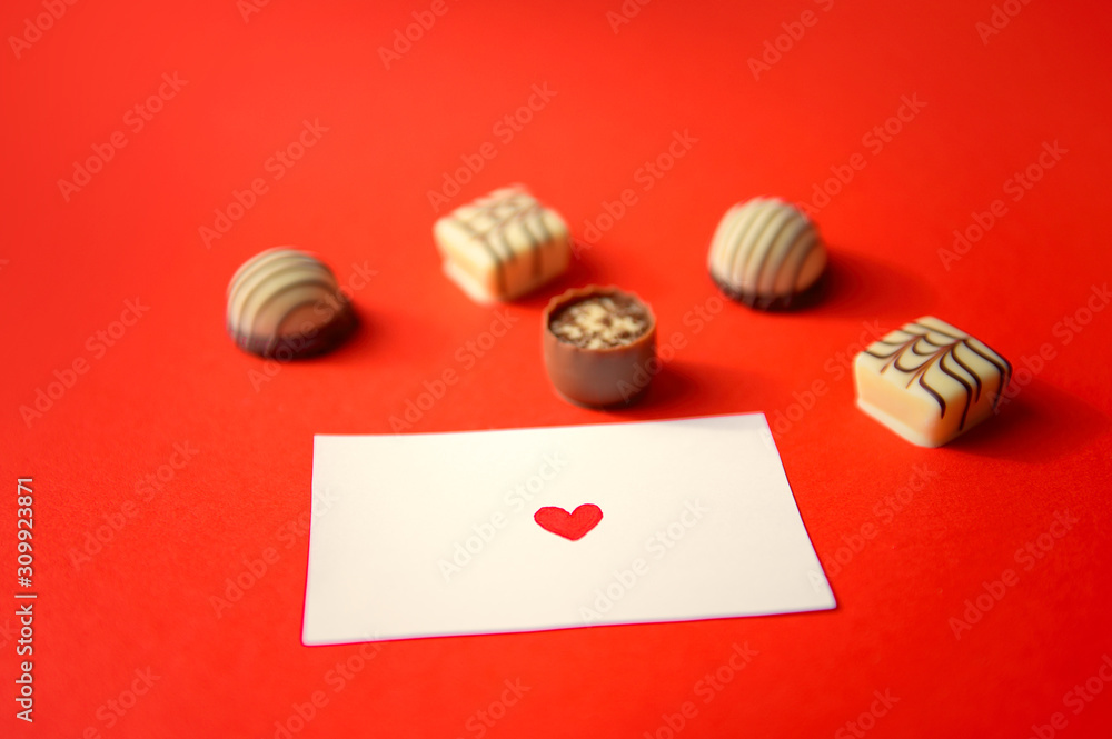St. Valentine's Day. Chocolate candies and a note with a heart on red background. Chocolate candies. Chocolate treats. Assorted chocolates. St. Valentine's Day. Chocolate candies and a note with a heart on red background. Chocolate candies. Chocolate treats. Assorted chocolates.