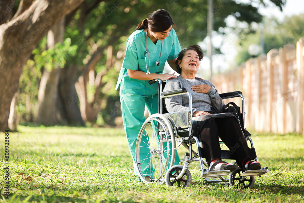 Asian senior woman sitting on the wheelchair with woman in doctor uniform in the park hospital Asian senior woman sitting on the wheelchair with woman in doctor uniform in the park hospital