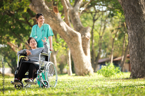 Asian senior woman sitting on the wheelchair with woman in doctor uniform in the park hospital