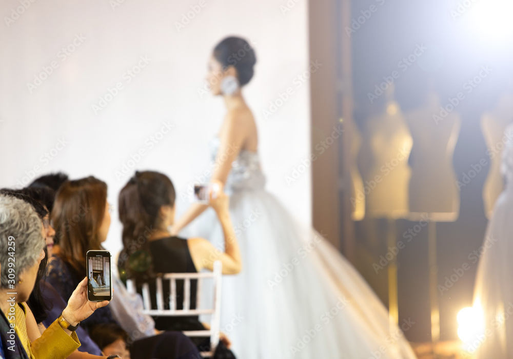 Fashion dress Model walk back on dark Runway Fashion Show catwalk along way finale, background stage ramp, selective focus, focus at audiences raise hand and use smartphone mobile phone take photo Fashion dress Model walk back on dark Runway Fashion Show catwalk along way finale, background stage ramp, selective focus, focus at audiences raise hand and use smartphone mobile phone take photo