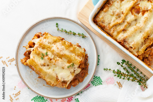 Cannelloni pasta with filling of ground beef, tomatoes, baked with bechamel tomato sauce and mozzarella. Classical Italian cuisine, white tablecloth with embroidery, rustic style, top view