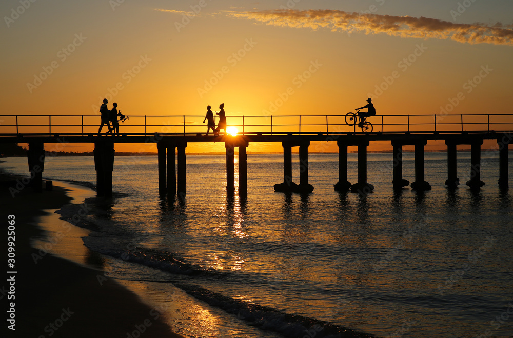 Naklejka premium Beachgoers on a jetty silhouetted against a golden summer sunset.