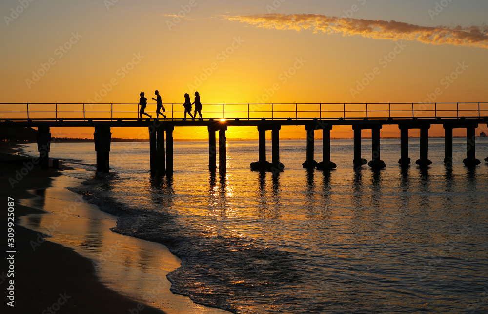 People silhouetted at sunset on jetty at a Mornington Peninsula beach near Melbourne Australia.