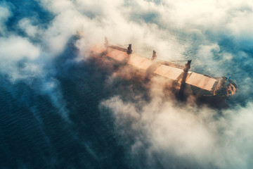 Cargo ship and cranes silhouettes in sea fog, crane vessel working for delivery of delivery containers.