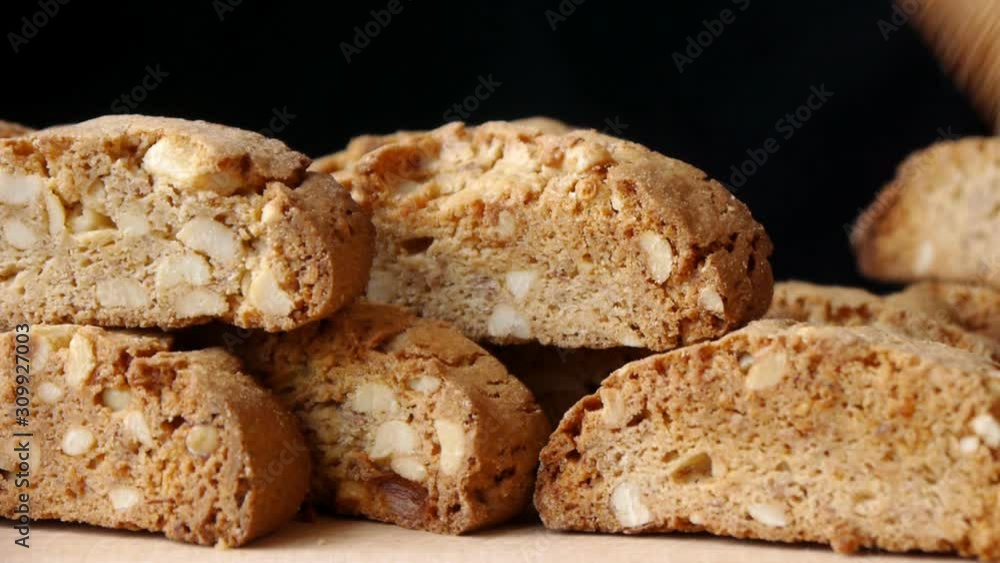 A female hand puts a Cantucci biscuit on a hill of cookies on a black background. A female hand puts a Cantucci biscuit on a hill of cookies on a black background.