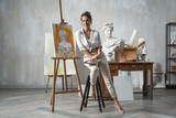 Satisfied female artist posing near new picture next to easel