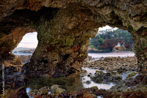 Large holes in the rock on stony coast near the Spanish Atlantic port city of Burela in Galicia. The mountain has two large stone arches. In the background the coastal landscape.
