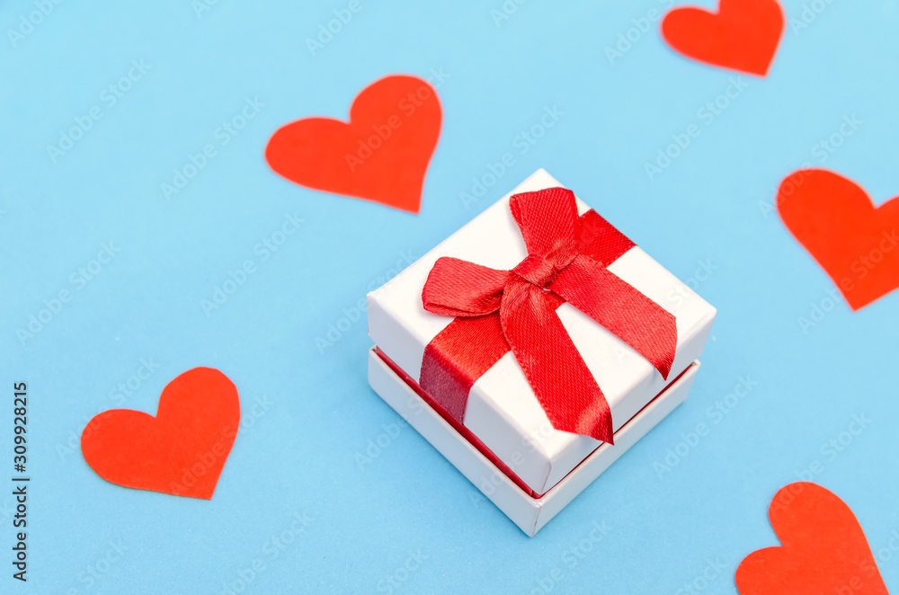 Gift box among red paper hearts on a blue background. Top view, copy space. Valentine's day, a symbol of love. Festive background
