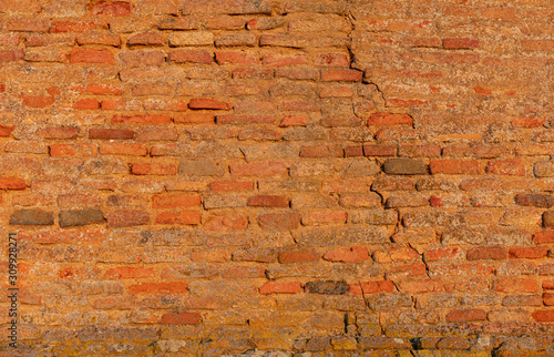A very old wall made of brick reddish stones. The old clinker wall has cracks and looks very antique. Interesting background with a retro look.