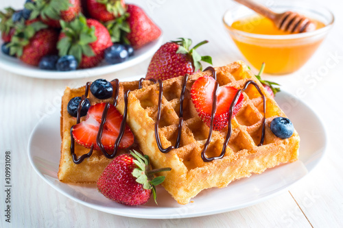Fresh homemade food of berry Belgian waffles with honey, chocolate, strawberry, blueberry, maple syrup and cream. Healthy dessert breakfast concept with juice