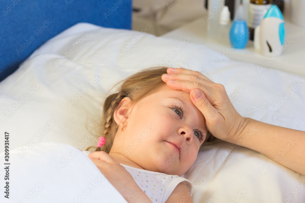 Woman hand on child forehead to feel temperature. Child in bed