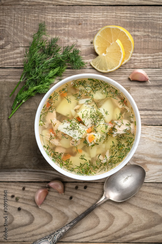 Fresh homemade fish soup with vegetables in bowl on rustic wooden background, top view with copy space.