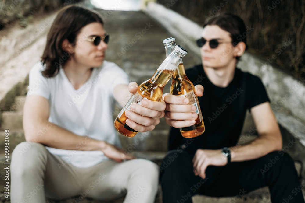 Two Stylish Twins Brothers Having Fun Drinking Beer on the Stairs Two Stylish Twins Brothers Having Fun Drinking Beer on the Stairs