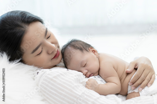 Young mother holding sleeping infant child on hands. Portrait of Asian young with her happy child on arms on white background.