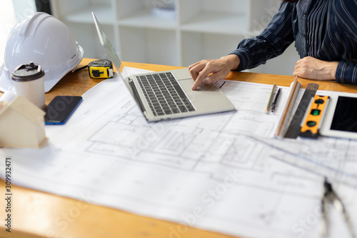 Top view, Architect or engineer hands working on blueprint plans with a laptop and pencil a ruler, calculator, and engineering tools. Architect or engineer working on blueprint in office.