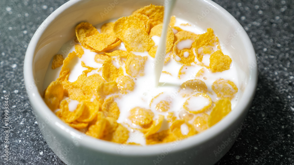 Preparing fast breakfast with cereal. Pouring milk in bowl with dry cornflakes. Traditional morning food. Preparing fast breakfast with cereal. Pouring milk in bowl with dry cornflakes. Traditional morning food.