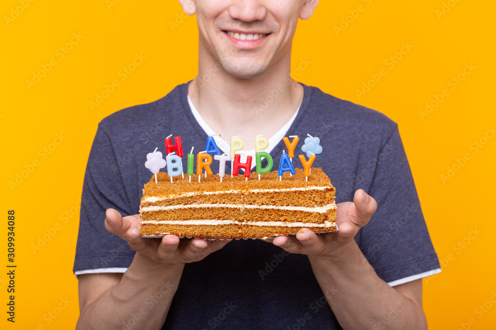 Close-up of man holding cakes happy birthday standing on a yellow background. Jubilee congratulations concept. Close-up of man holding cakes happy birthday standing on a yellow background. Jubilee congratulations concept.