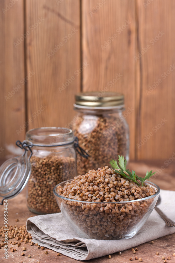 Cooked buckwheat in a glass, transparent bowl, parsley leaf, linen napkin, jars for storing cereals Cooked buckwheat in a glass, transparent bowl, parsley leaf, linen napkin, jars for storing cereals