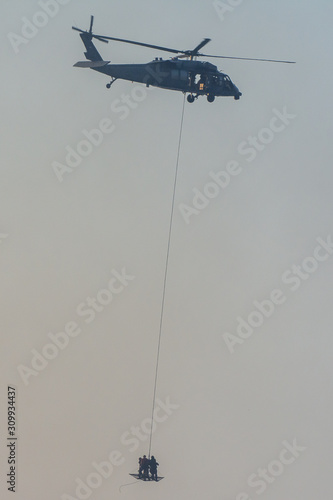 Military team in conflict resucing people by helicopter. flying through the air on a rope attached to chopper in the smoke and haze in the MIddle East conflict.