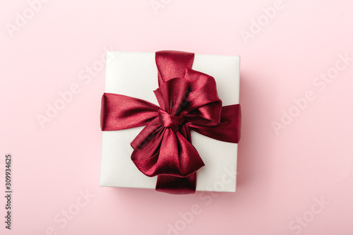 White gift box, with burgundy satin ribbon, pink background, top view