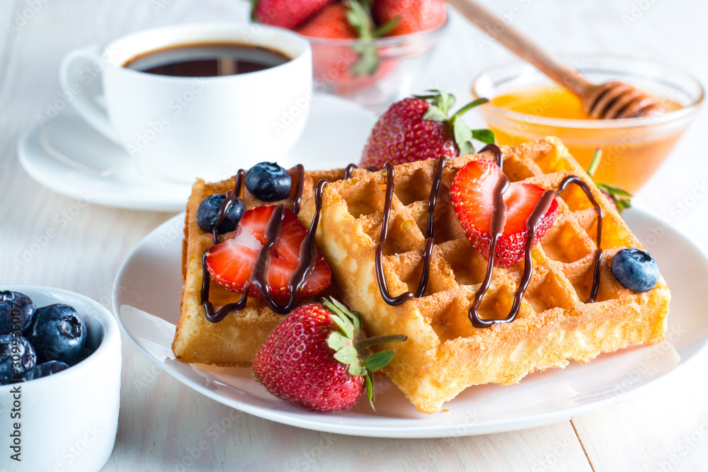 Fresh homemade food of berry Belgian waffles with honey, chocolate, strawberry, blueberry, maple syrup and cream. Healthy dessert breakfast concept with juice