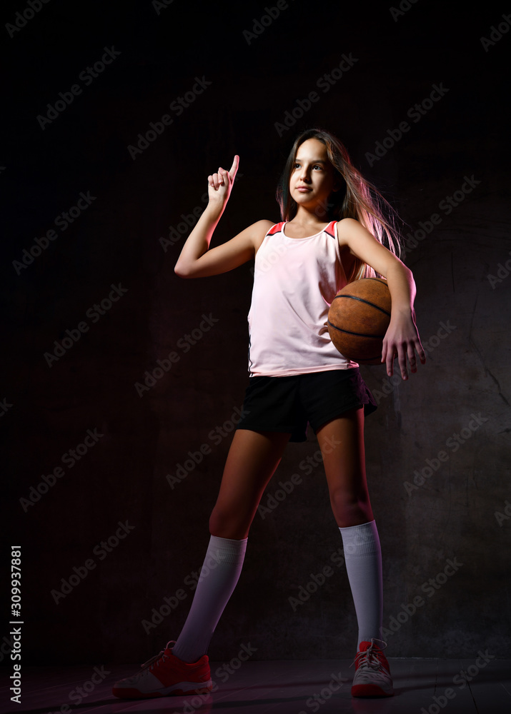 Beautiful caucasian teen woman in sportswear playing basketball . Sport concept isolated on black background.