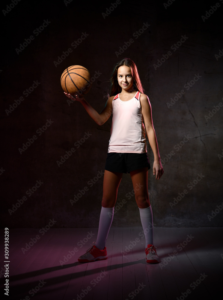 Naklejka premium Beautiful caucasian teen woman in sportswear playing basketball . Sport concept isolated on black background.