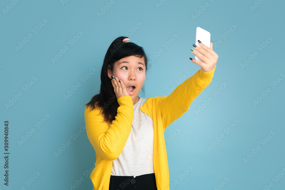 Asian teenager's portrait isolated on blue studio background. Beautiful female brunette model with long hair. Concept of human emotions, facial expression, sales, ad. Making selfie or vlog. Asian teenager's portrait isolated on blue studio background. Beautiful female brunette model with long hair. Concept of human emotions, facial expression, sales, ad. Making selfie or vlog.