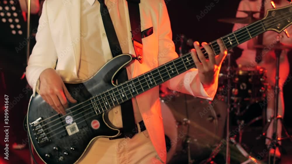 Young handsome man in a suit plays black bass guitar on stage filled with red Young handsome man in a suit plays black bass guitar on stage filled with red