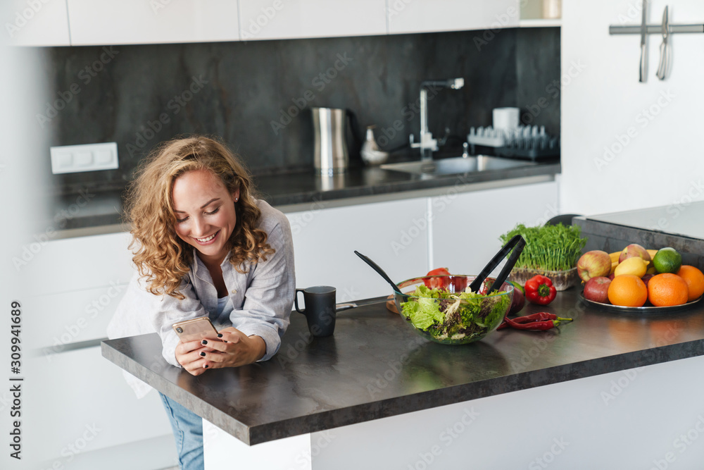 Smiling young woman using smartphone in kitchen Smiling young woman using smartphone in kitchen