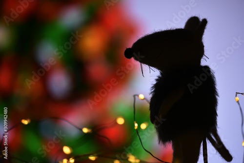 Dark silhouette of a rat on a background of abstract decorated blurry Christmas tree.