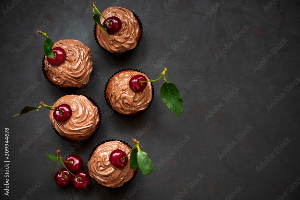 Top view chocolate cupcakes with ripe red cherries and cheese cream on dark wooden background. Selective focus. Healthy food Top view chocolate cupcakes with ripe red cherries and cheese cream on dark wooden background. Selective focus. Healthy food
