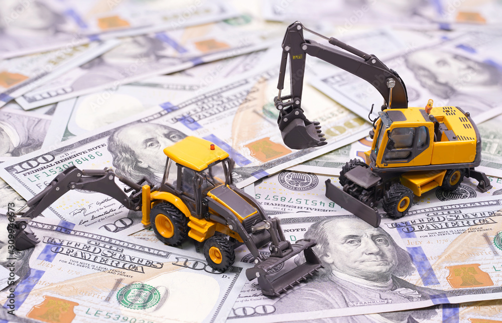 Fototapeta premium yellow tractor and excavator. miniature models in dollars